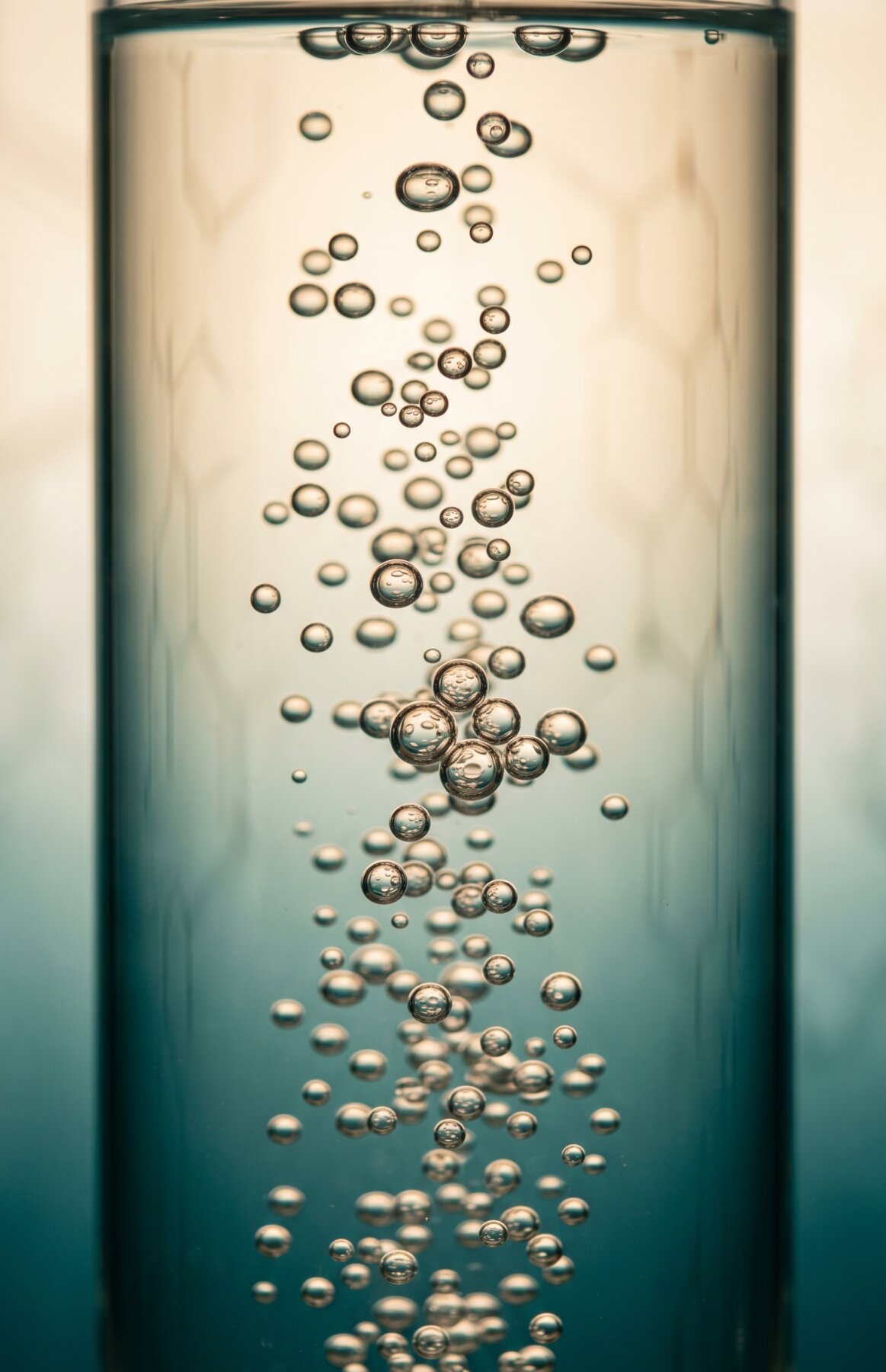 Backlit teal hydrogen bubbles rising through a tall glass vessel, warm to cool gradient