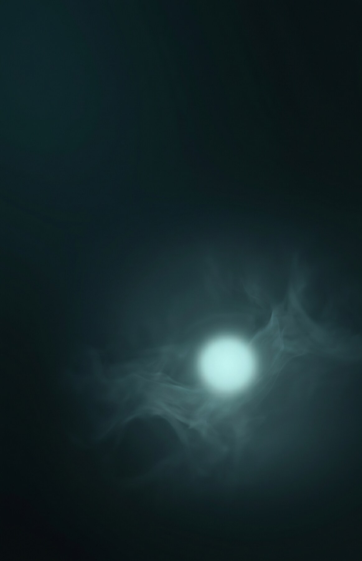 A single point of pale teal light glowing in deep dark space, evoking a quiet particle suspended in stillness.